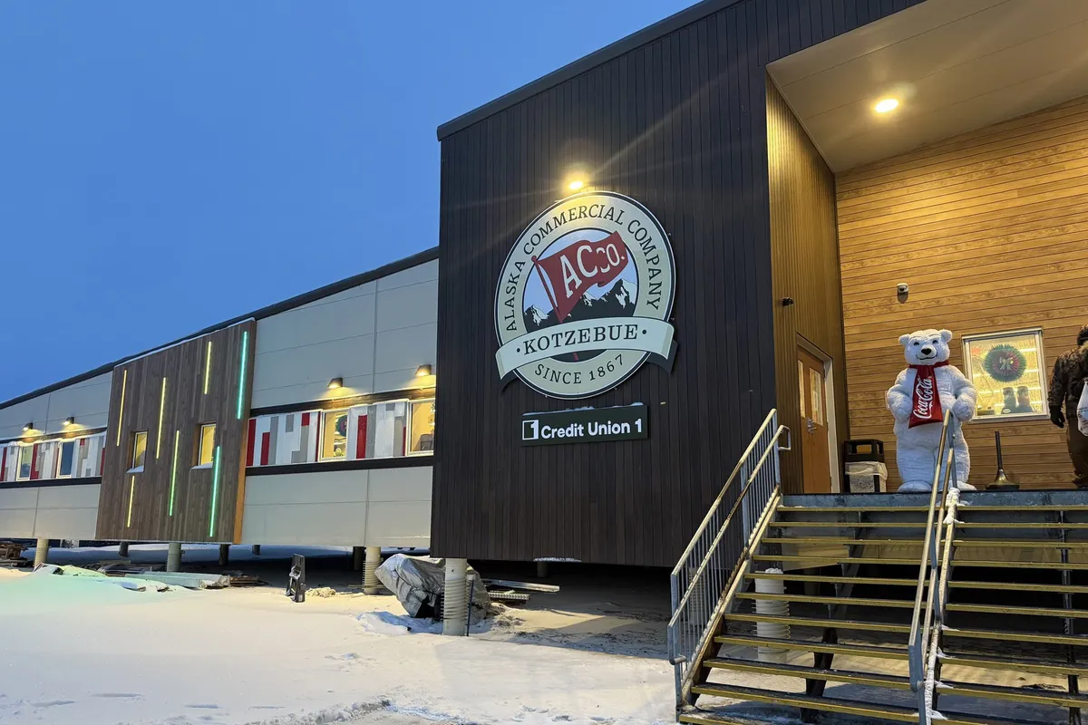 Entrance to the new AC grocery store in Kotzebue at dusk, with snow on the ground and a mascot costume on the stairs