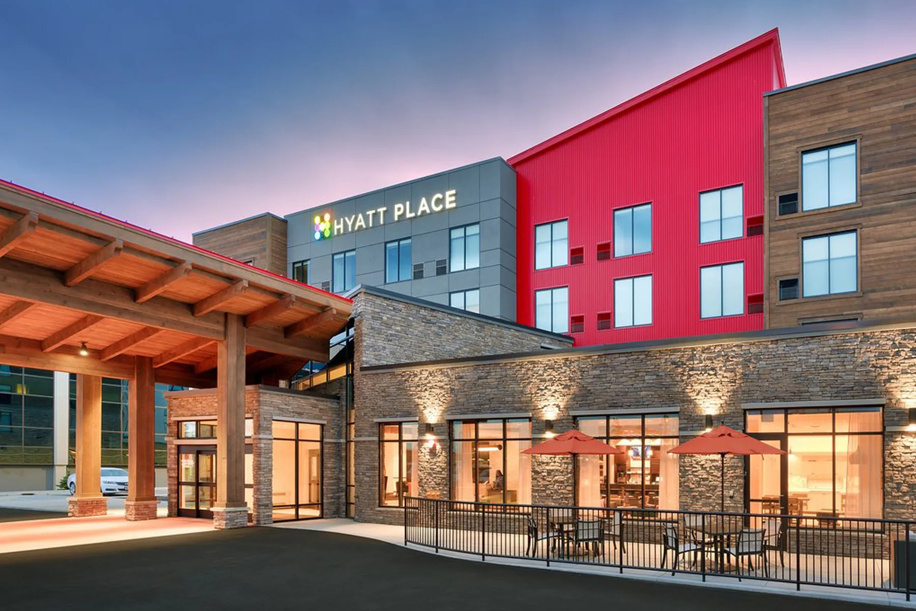 Hyatt Place Anchorage at dusk with its red facade, timber entry canopy and lit patio
